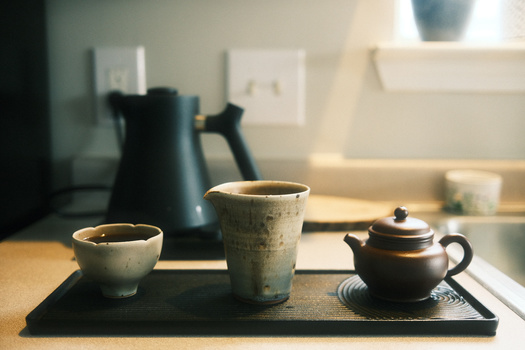 Ceramic tea service arranged on a black tray with soft natural window lighting.