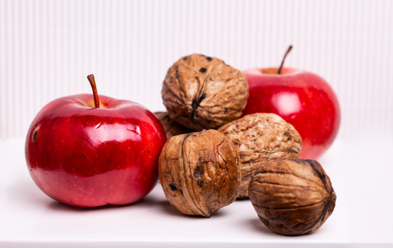 Two red apples and three walnuts in shells arranged on a white surface.