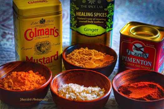 Spice bottles and bowls arranged with ground spices in warm studio lighting against a textured blue background.