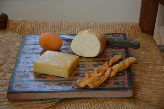 Cheese and bread arranged on a blue decorative cutting board with a knife and pretzel stick.