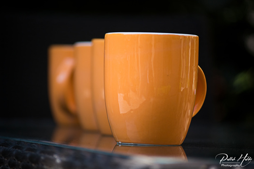 Row of orange ceramic mugs with handles in sharp focus against a dark blurred background.