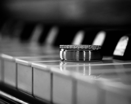 Two wedding rings positioned on a piano keyboard in black and white.
