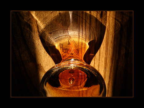 Hands holding a glowing amber glass vessel against wooden background with dramatic backlighting.
