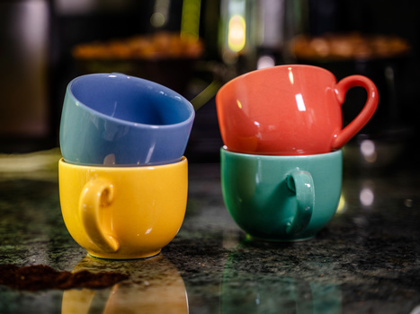 Two colorful stacked ceramic cups with handles photographed on a dark speckled surface with warm backlighting.