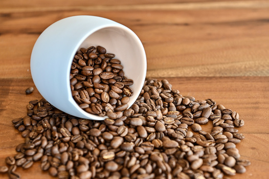 White ceramic cup tipped over on wooden surface with coffee beans spilling out.