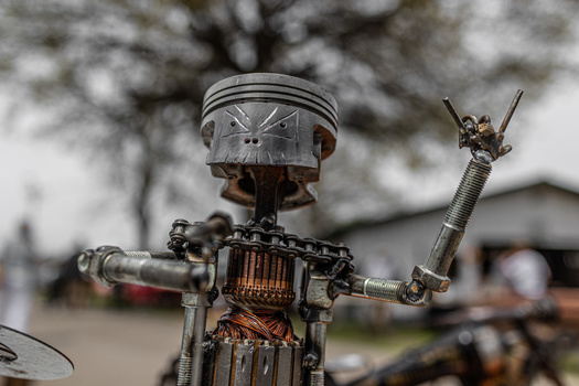 Steampunk robot sculpture made from mechanical parts and a clock face, with arm raised in peace gesture.