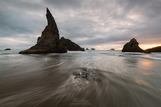 Dramatic rock formations rise from shallow ocean water during twilight with long exposure blur effect.