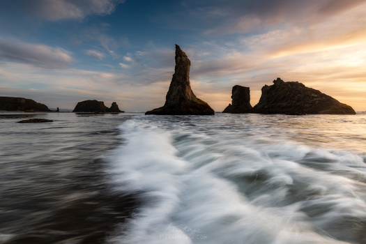 Dramatic rock formations rising from turbulent ocean waves at sunset with warm golden light.