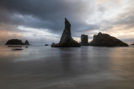 Dramatic rocky sea stacks rising from shallow ocean waters under stormy clouds at twilight.