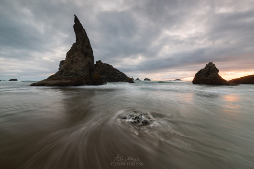 Dramatic sea stacks rising from a long-exposure beach at twilight with swirling water movement.