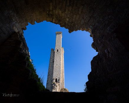 Stone tower framed through a dark archway opening against blue sky.