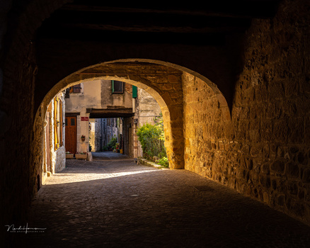 Stone archway framing a sunlit Mediterranean street with warm golden light.