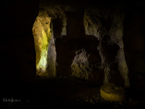 Silhouetted figure standing in an ancient stone archway lit by warm golden light from above.