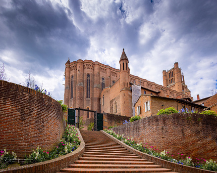 Brick staircase leading to a terracotta-colored church building with bell tower against dramatic cloudy sky.