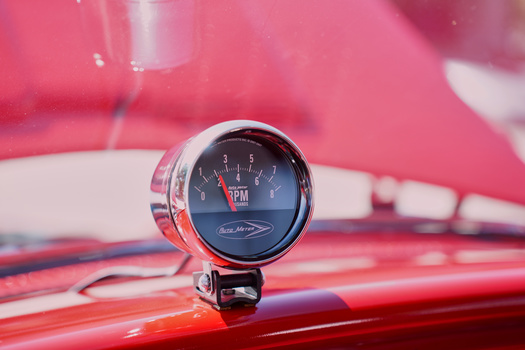 Classic analog tachometer gauge mounted on red vintage car dashboard.