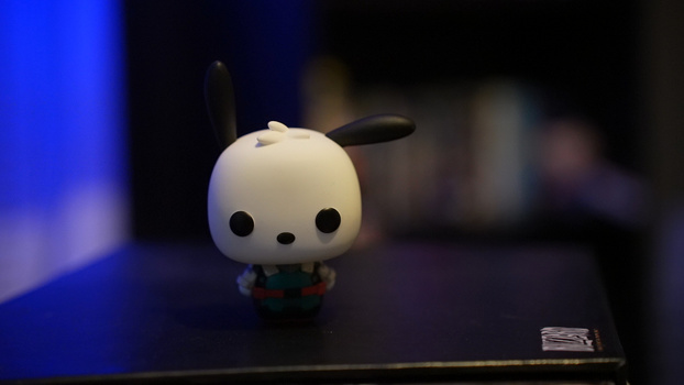 White ceramic figurine with black dot eyes and black ears against a blurred blue and dark background.