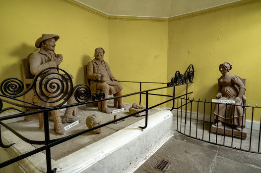 Museum diorama with clay figurines and decorative ironwork arranged in a yellow room.