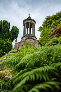 Stone tower with domed cupola surrounded by lush green foliage and cypress trees.