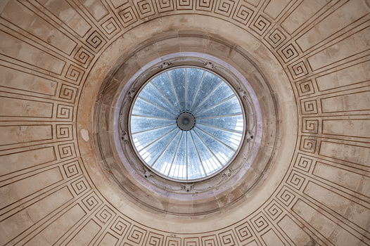 Circular dome ceiling with geometric Greek key pattern radiating toward a blue-tinted skylight at center.