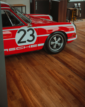Red race car with number 23 displayed on door, shown in an indoor showroom with wooden flooring.