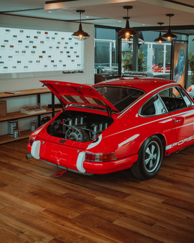 Red vintage sports car with hood open, displaying engine, parked indoors on wooden flooring.