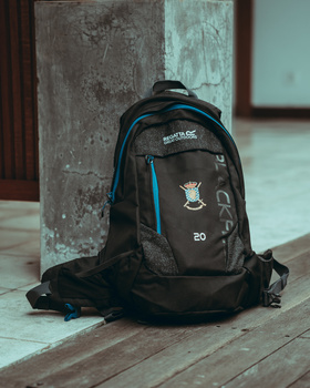 Black and blue backpack with camera gear sitting on a tiled floor against weathered concrete columns.