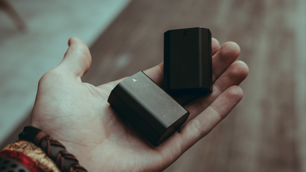Hand holding two black rectangular objects against a neutral background.
