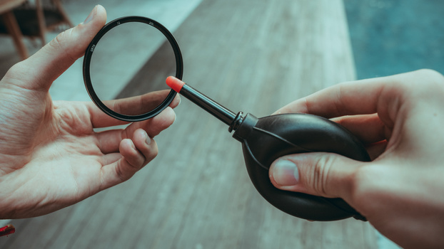 Two hands holding a magnifying glass with an orange accent against a blurred wooden background.