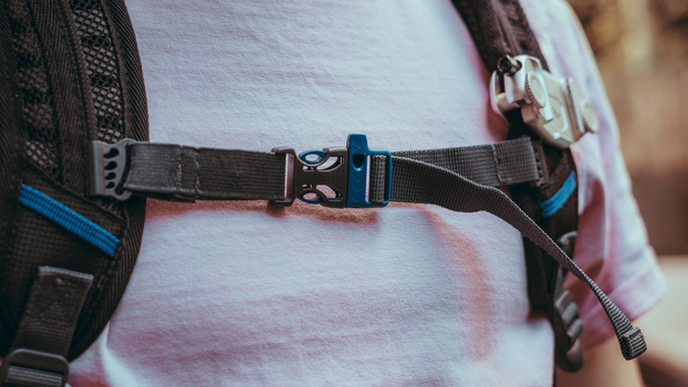 Close-up of a climbing harness waist belt with blue accents and carabiners worn over a white t-shirt.