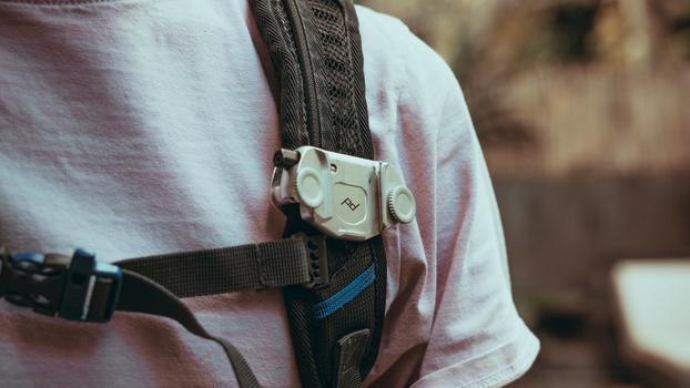 White camera strap attachment clipped to a black camera strap worn over a pink shirt.