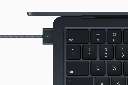 Close-up of a USB-C cable connected to the side of a laptop keyboard, with a green indicator light visible.