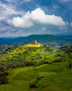 Medieval castle perched on a green hilltop overlooking a verdant valley landscape.