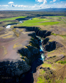 Aerial view of a river canyon cutting through vast moorland with green valleys and distant mountains.
