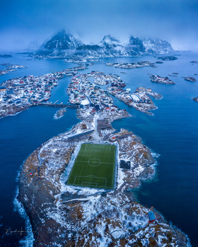 Aerial view of a snow-covered archipelago with a soccer field on the largest island surrounded by blue water.