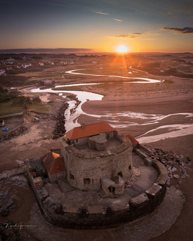 Medieval stone fortress surrounded by winding river at golden hour sunset.
