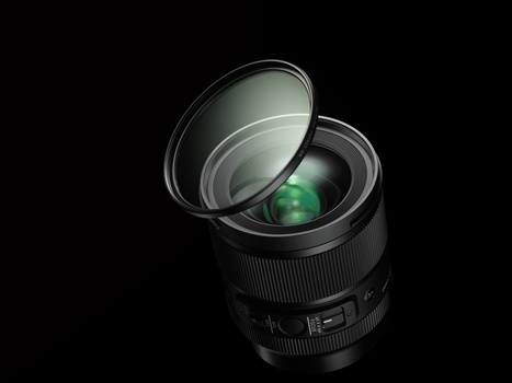 Camera lens with front element removed, showing internal green-tinted glass optics and mechanical components against black background.