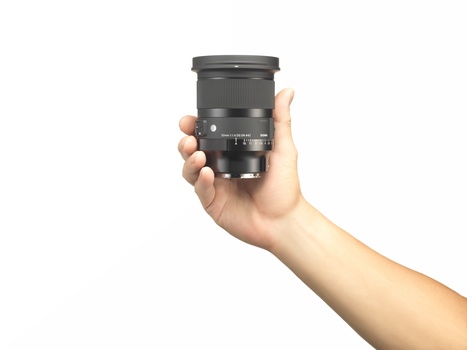 Hand holding a telephoto zoom lens with dark gray finish and focus ring visible.