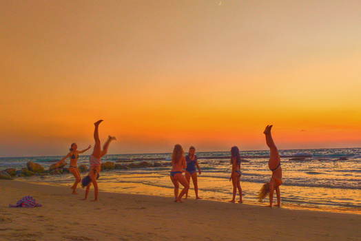 Group of people doing handstands and cartwheels on a beach at sunset.