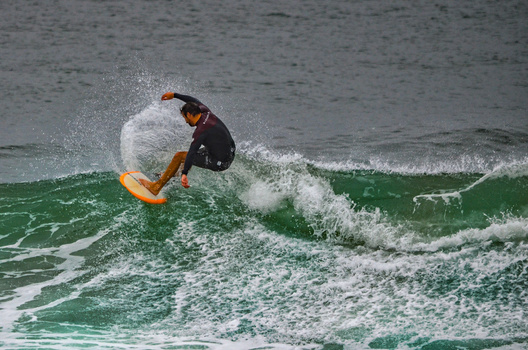 Surfer riding a green wave in a dynamic maneuver with water spray.
