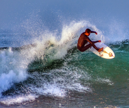 Surfer riding a wave in shallow water, performing a maneuver with spray cascading around the board.