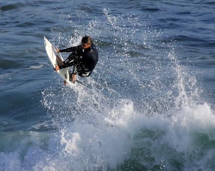 Surfer executing a radical cutback maneuver on a wave, with water spray backlit by bright sunlight.