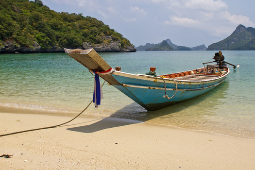 Traditional wooden longtail boat anchored in shallow turquoise water near a sandy beach.