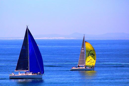 Two sailboats with full sails on calm blue water under clear sky.