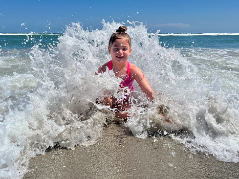 Young child in pink swimsuit playing in ocean waves at the beach on a sunny day.