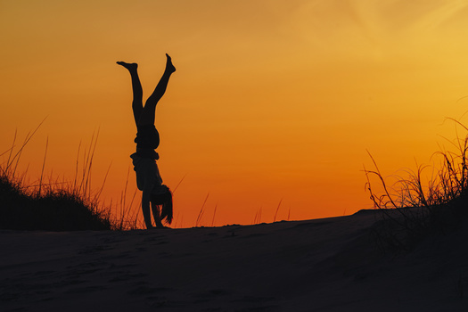 Silhouetted figure performing a handstand on a sand dune at sunset.