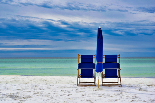 Two navy beach chairs and an umbrella arranged symmetrically on white sand facing turquoise water.