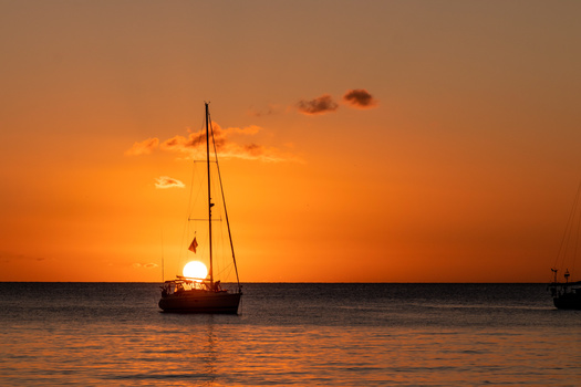 Sailboat silhouetted against an orange sunset over calm water.