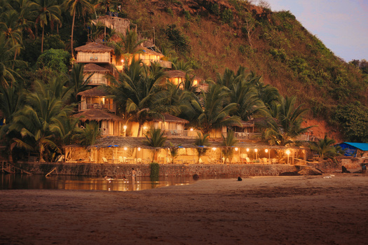 Beachfront resort buildings lit by golden hour light against a steep forested hillside.