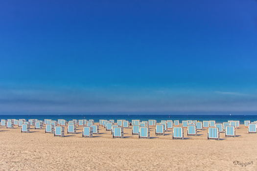 Rows of blue and white striped beach huts line a sandy beach under clear blue sky.