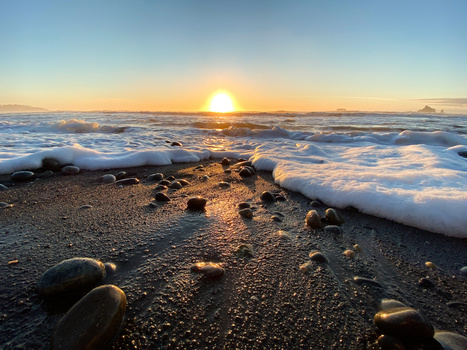 Sun rising over ocean waves with rocks scattered across wet sand beach.
